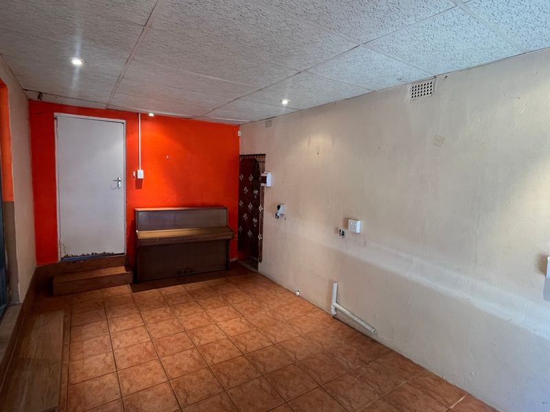 An empty, tiled living area featuring a drop ceiling, recessed lighting, and a distinct orange accent wall, ready for renovation or staging.