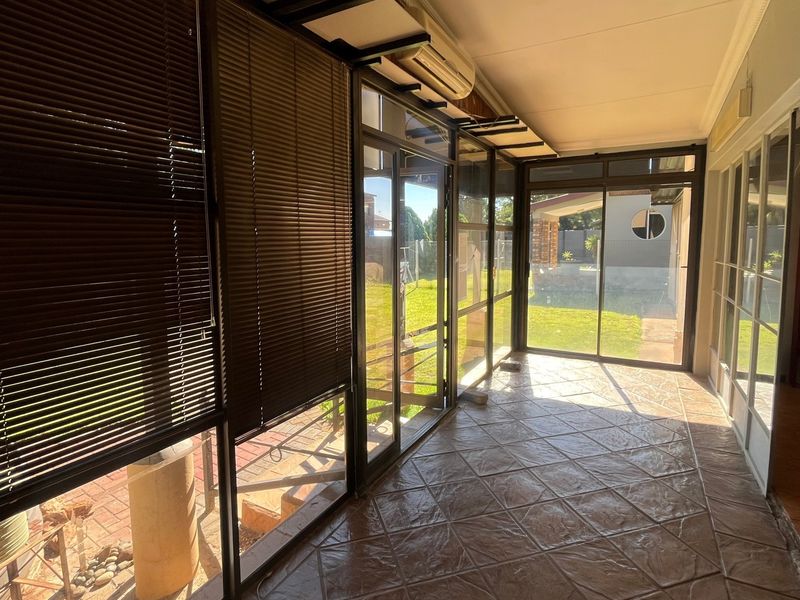 A spacious enclosed patio featuring tiled flooring, large sliding glass doors, and wall-mounted air conditioning, offering a bright transition space to the garden.