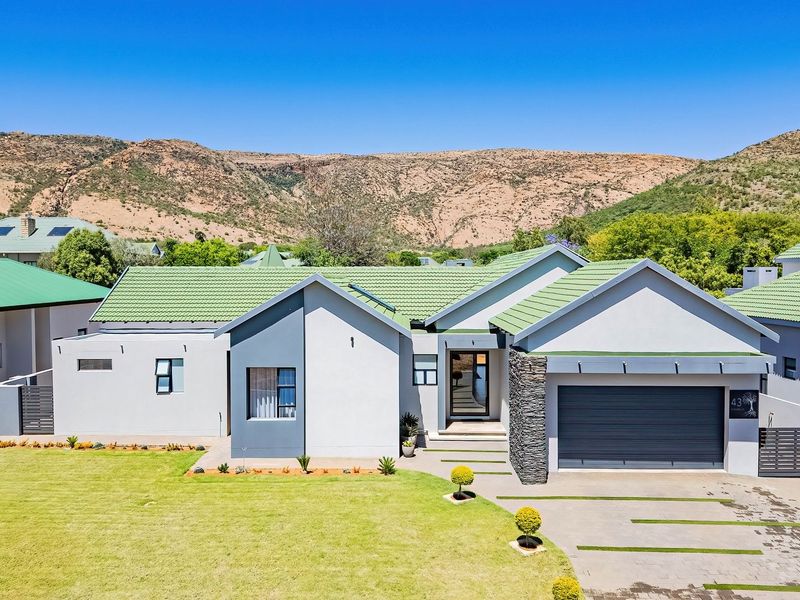 A modern single-story residential home featuring a tiled roof, stone-clad accents, a double garage, and a well-maintained front lawn with a paved driveway.