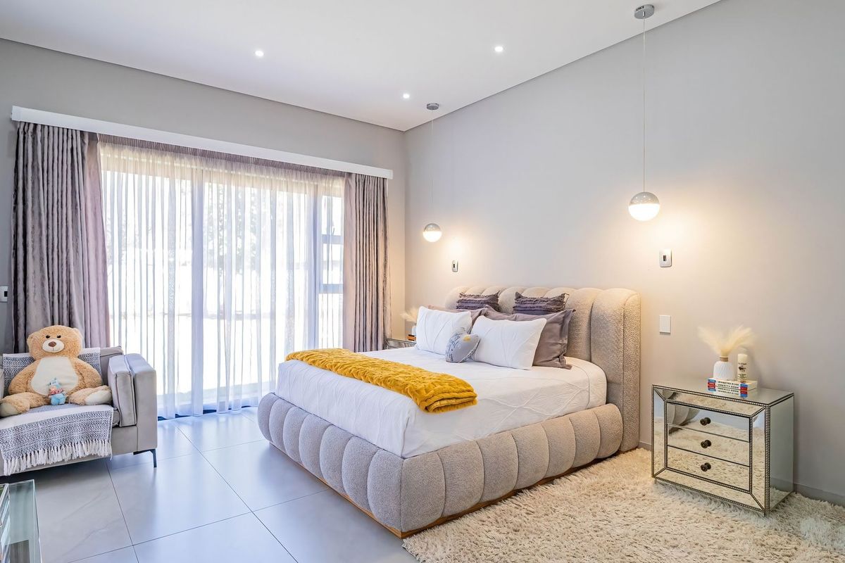 A modern, well-lit bedroom featuring tiled flooring, recessed downlighting, pendant bedside lights, and a large sliding glass door providing natural light.