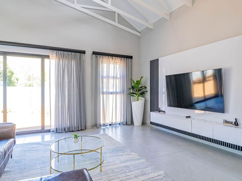 Modern living room featuring a vaulted ceiling with exposed trusses, large sliding glass doors for natural light, and a sleek built-in media console.