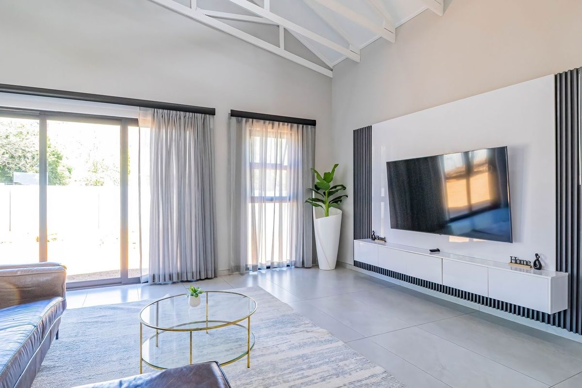 Modern living room featuring a vaulted ceiling with exposed trusses, large sliding glass doors for natural light, and a sleek built-in media console.