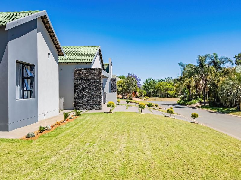 A well-maintained residential exterior featuring modern grey facades, stone cladding accents, green tiled roofing, and a neatly landscaped front lawn.