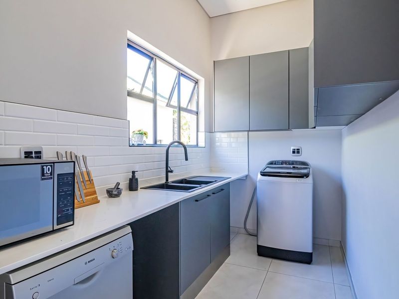 Modern laundry room featuring sleek grey cabinetry, white quartz countertops, subway tile backsplash, and a contemporary black sink and faucet.