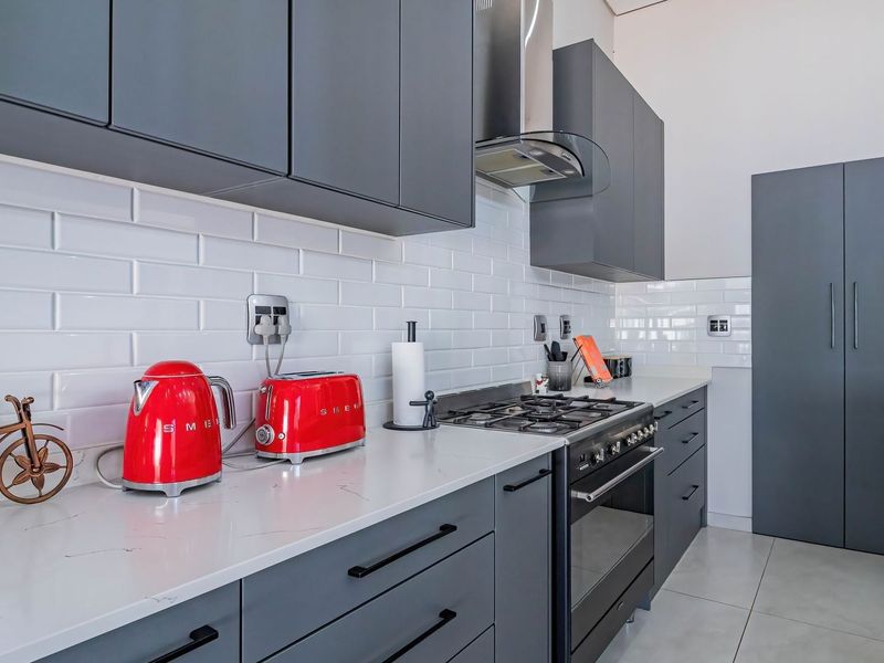 Modern kitchen featuring sleek grey cabinetry, white subway tile backsplash, stone countertops, and high-quality built-in gas cooking appliances.