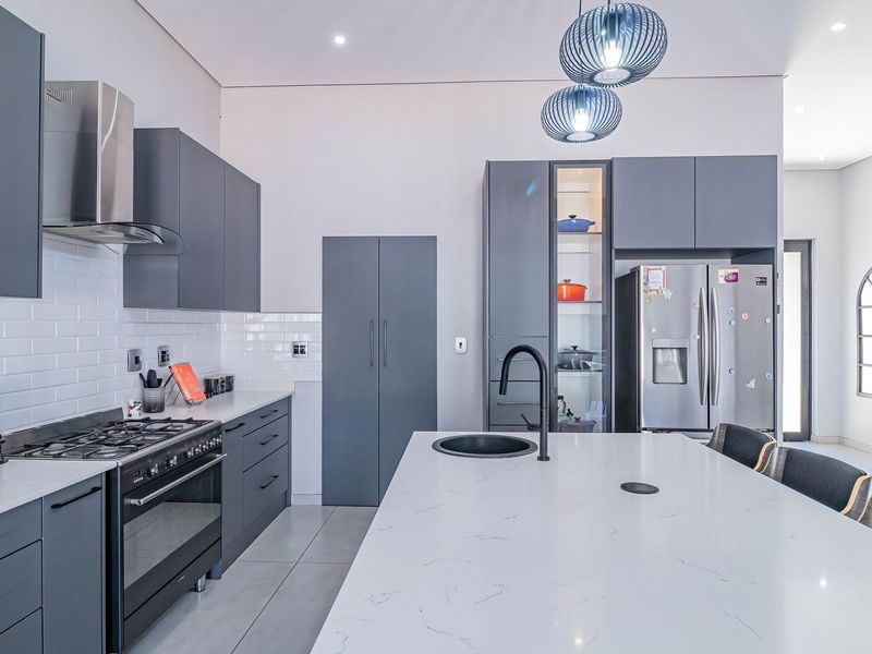 Modern kitchen featuring dark grey cabinetry, white quartz countertops, a central island with a sink, and high-end built-in appliances.