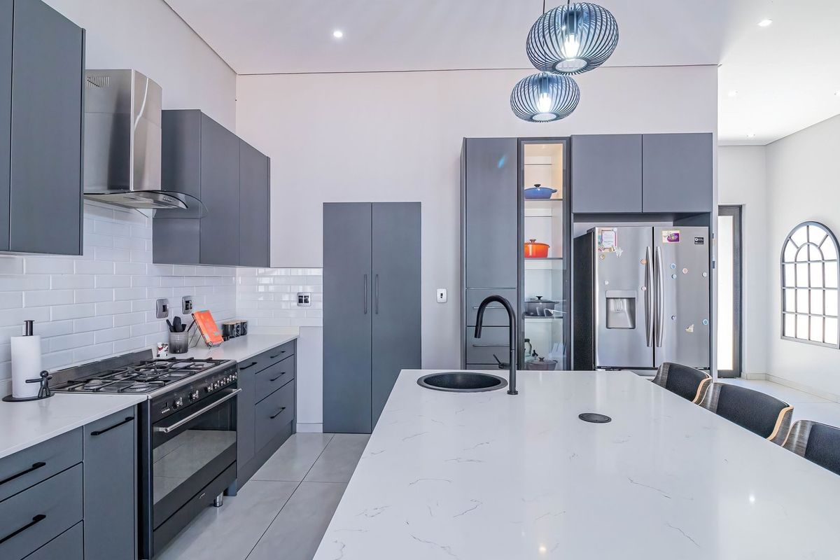 Modern kitchen featuring dark grey cabinetry, white quartz countertops, a central island with a sink, and high-end built-in appliances.
