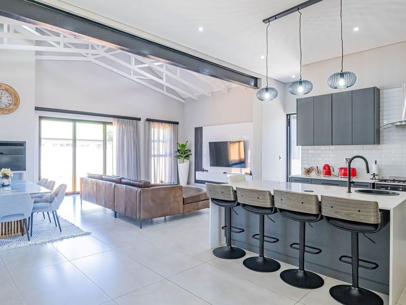 Spacious open-plan living area featuring a modern kitchen with a central island, vaulted ceilings with exposed beams, and seamless flow to the outdoor patio.