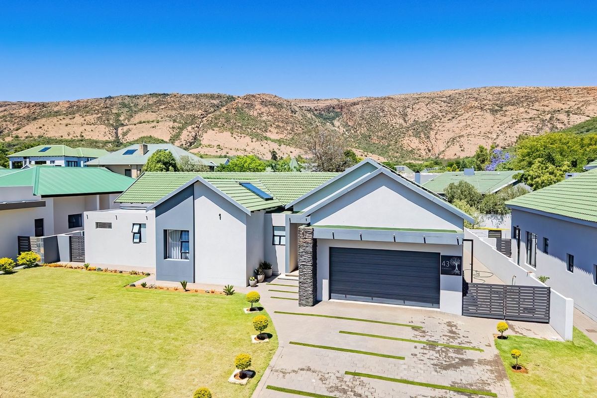 Aerial view of a modern residential property featuring a tiled roof, stone-clad accents, a paved driveway, and a well-maintained lawn against a mountain backdrop.