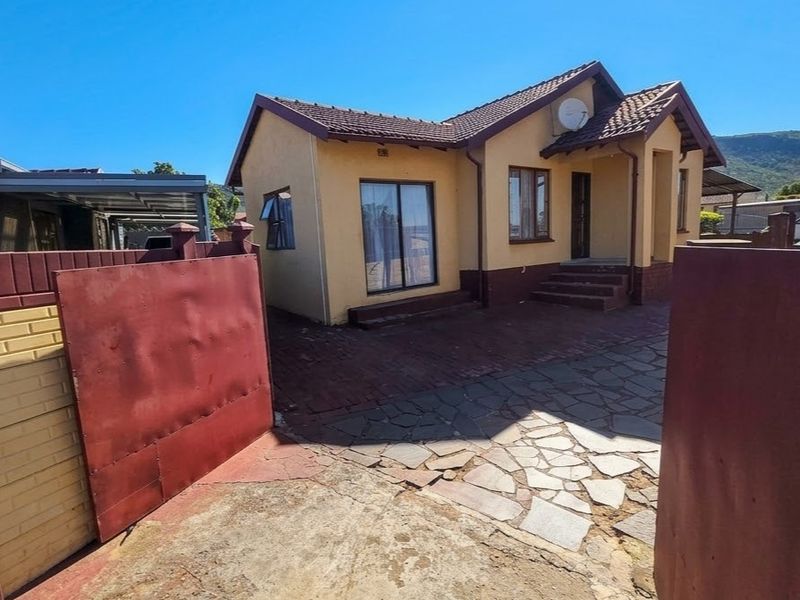 Front view of a single-story house featuring a tiled roof, paved driveway, and secure boundary wall with a metal gate.