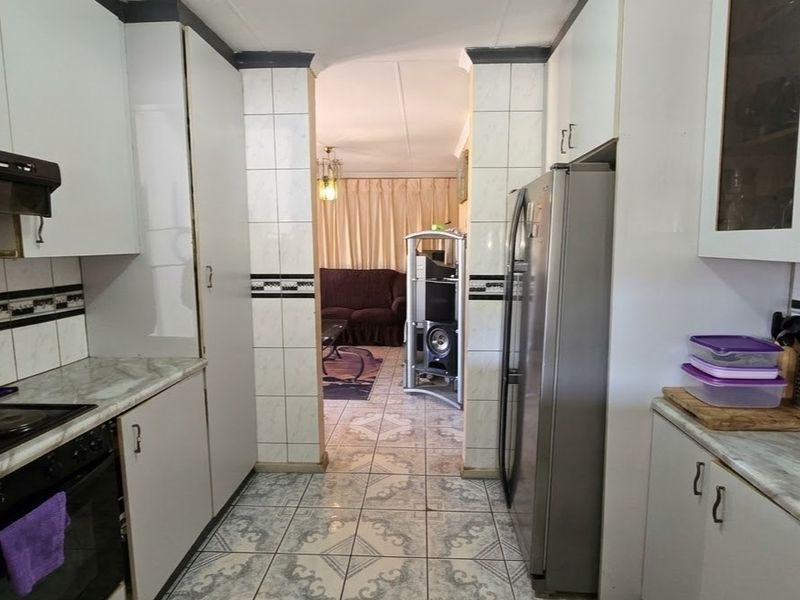 Functional kitchen featuring built-in cabinetry, tiled backsplash, and integrated appliances, with a direct walkway leading into the adjacent living area.
