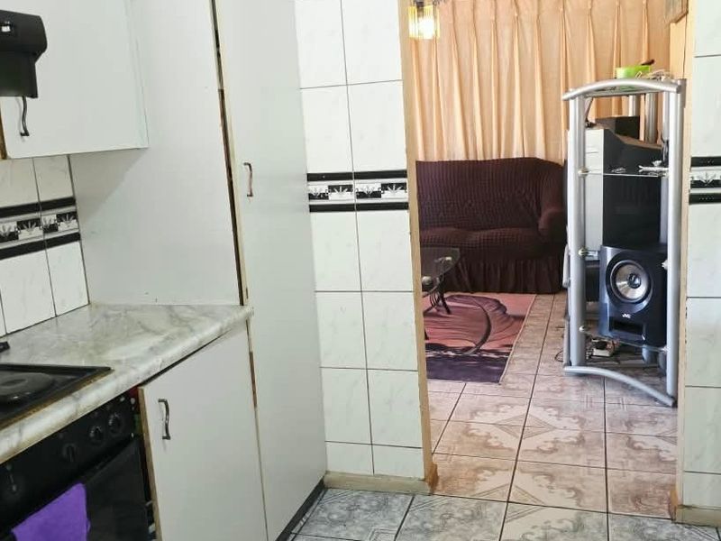 A functional kitchen featuring built-in cabinetry, an electric stove with extractor fan, and tiled finishes, leading into an adjacent living area.