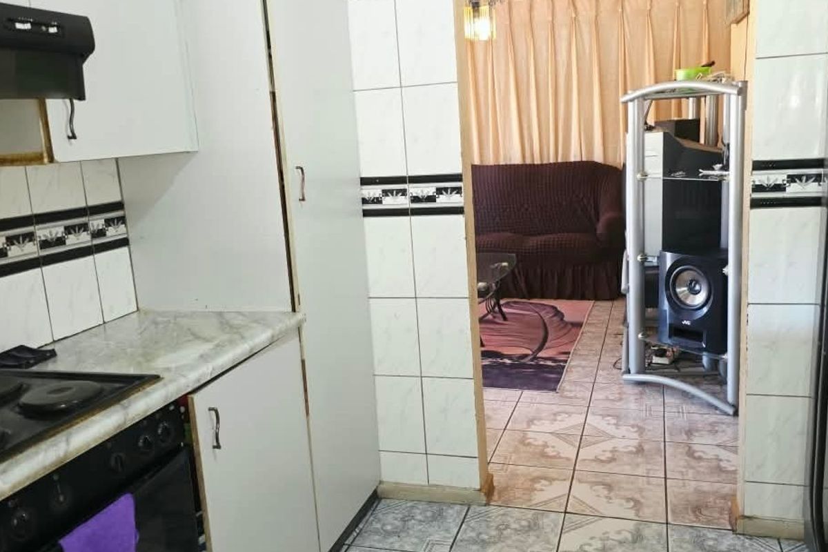 A functional kitchen featuring built-in cabinetry, an electric stove with extractor fan, and tiled finishes, leading into an adjacent living area.