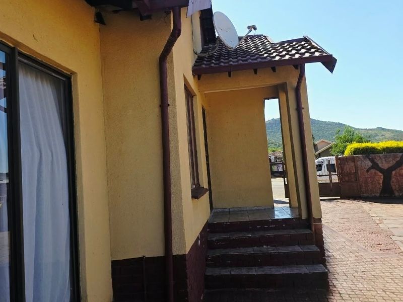 Front exterior view of the house featuring a tiled roof entrance, brick steps, and a paved driveway area.