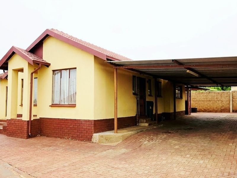 Front view of a single-story house featuring a tiled roof, brick base, and an attached carport with a paved driveway.