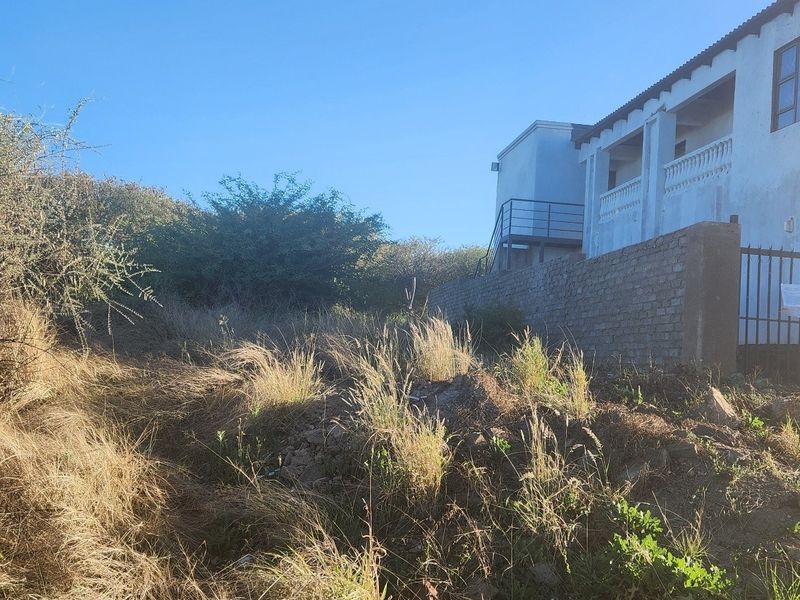 View of the rear exterior of the property featuring a brick boundary wall, metal gate, and an elevated balcony with an external staircase.