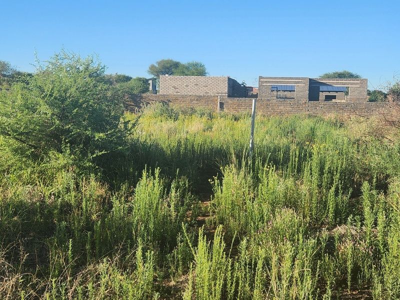 Vacant commercial land featuring overgrown vegetation and a partially constructed masonry building structure at the rear boundary.
