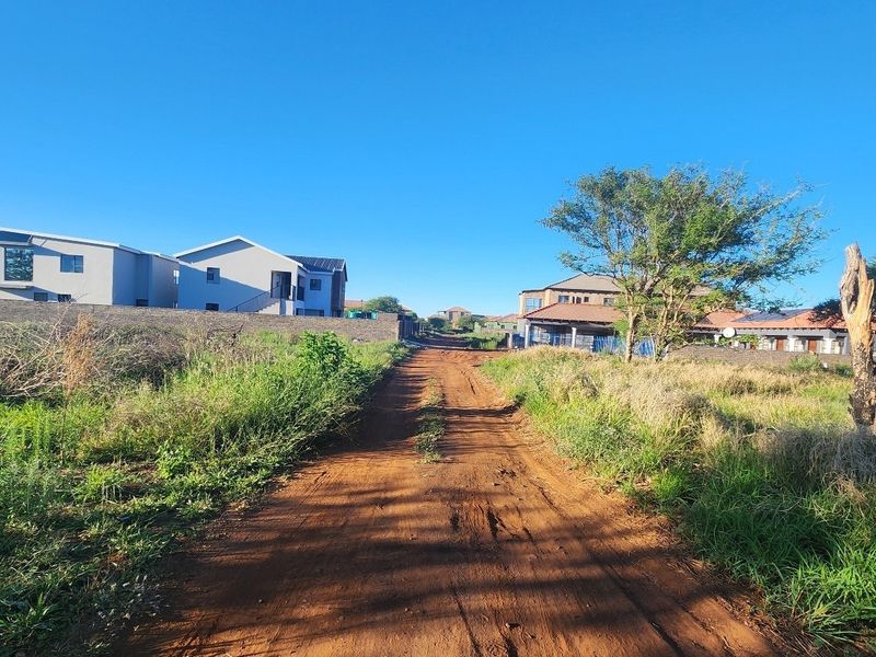 A view of an unpaved access road leading through a developing residential area with established neighboring properties.