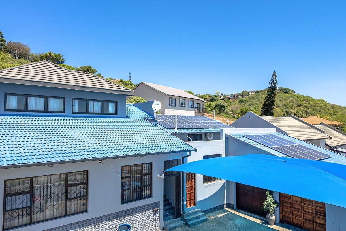 Rear exterior view of the property featuring a tiled roof, installed solar panels, stone cladding accents, and a covered parking area with a shade sail.