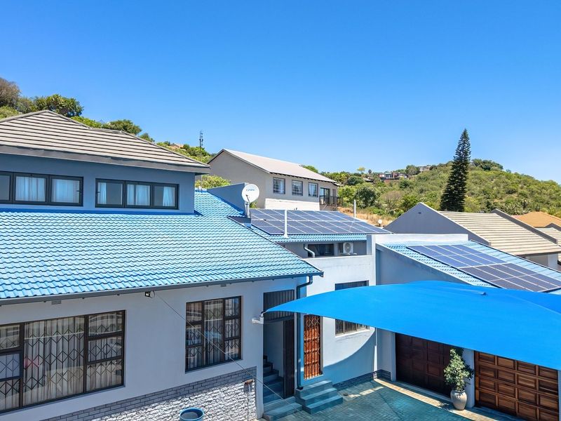 Rear exterior view of the property featuring a tiled roof, installed solar panels, stone cladding accents, and a covered parking area with a shade sail.
