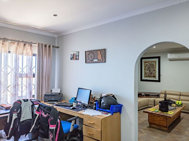 A functional home office space featuring an arched entryway leading to an adjacent living area, equipped with recessed lighting and a wall-mounted air conditioner.
