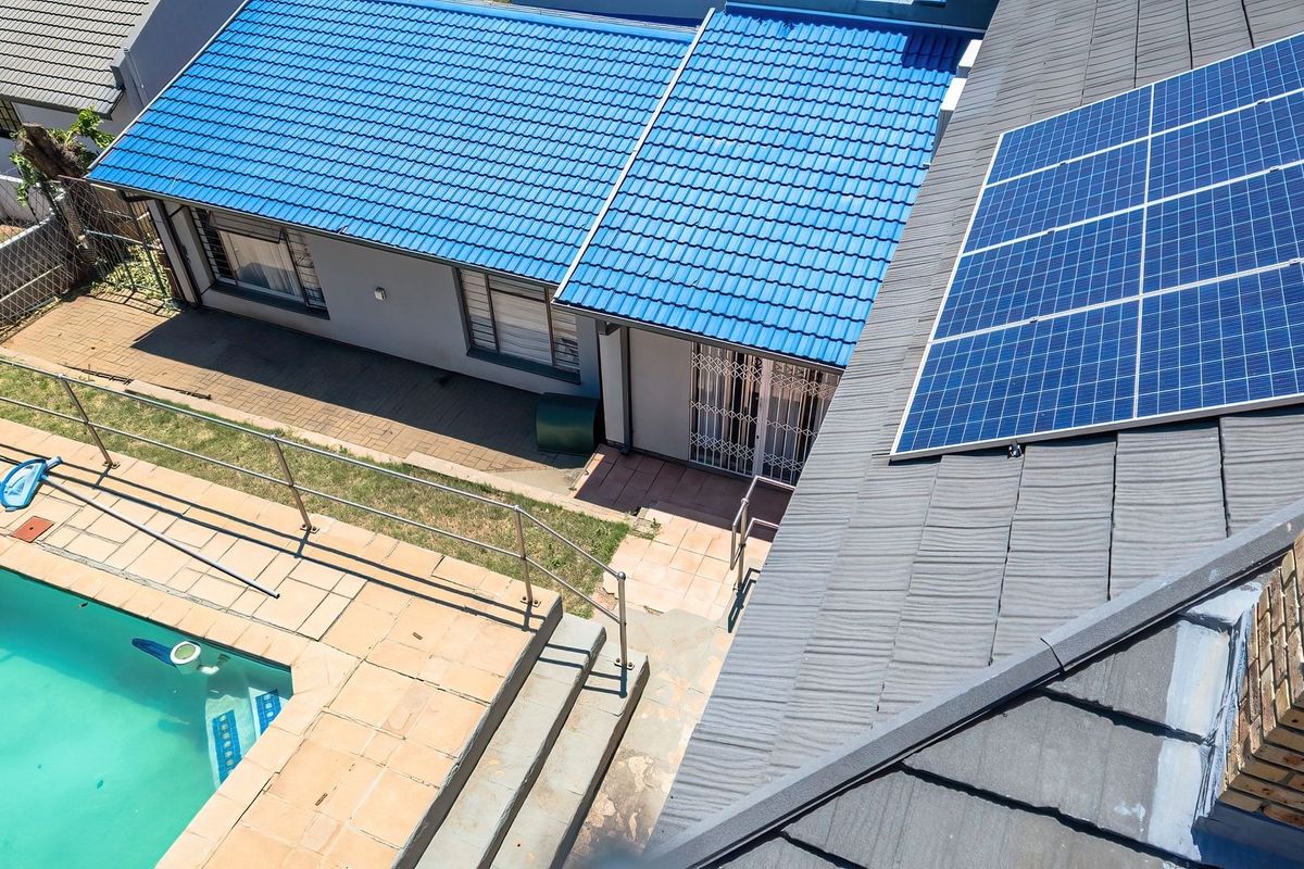 Aerial view of the property featuring a tiled roof with solar panels, a swimming pool, and a paved patio area.