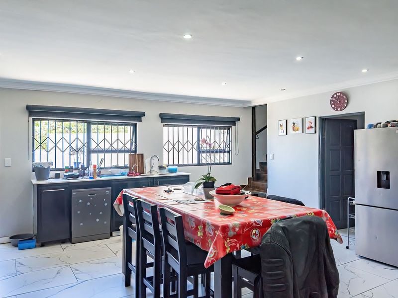An open-plan kitchen and dining area featuring modern marble-look floor tiles, recessed downlighting, and functional cabinetry with integrated appliances.