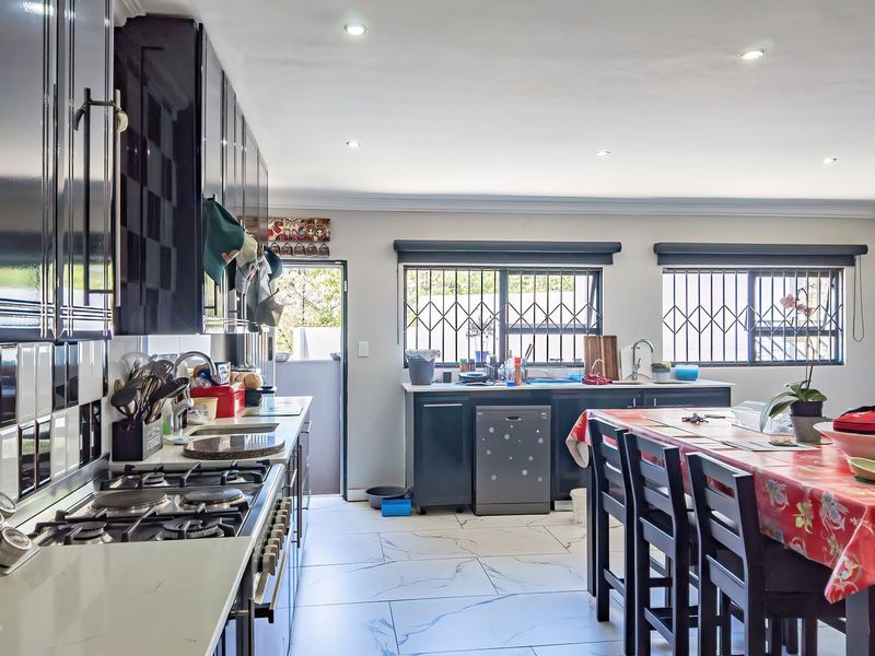 Spacious kitchen featuring modern black cabinetry, stone countertops, gas hob, and tiled flooring with integrated dining area and security bars on windows.