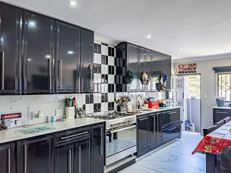 Modern kitchen featuring high-gloss black cabinetry, a gas hob with built-in oven, checkered tile backsplash, and marble-look flooring with direct access to the exterior.