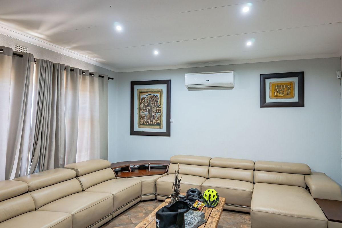 A well-maintained living room featuring recessed downlighting, tiled flooring, and a wall-mounted split-system air conditioning unit.