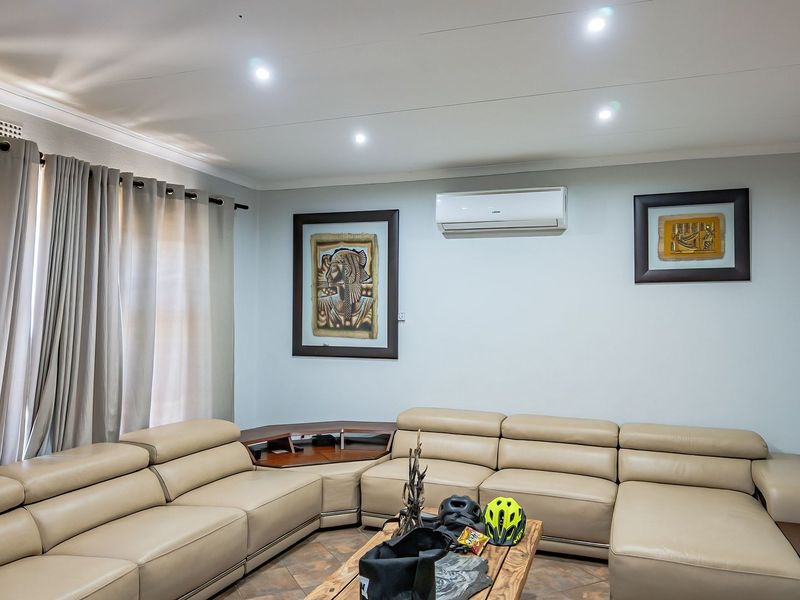 A well-maintained living room featuring recessed downlighting, tiled flooring, and a wall-mounted split-system air conditioning unit.