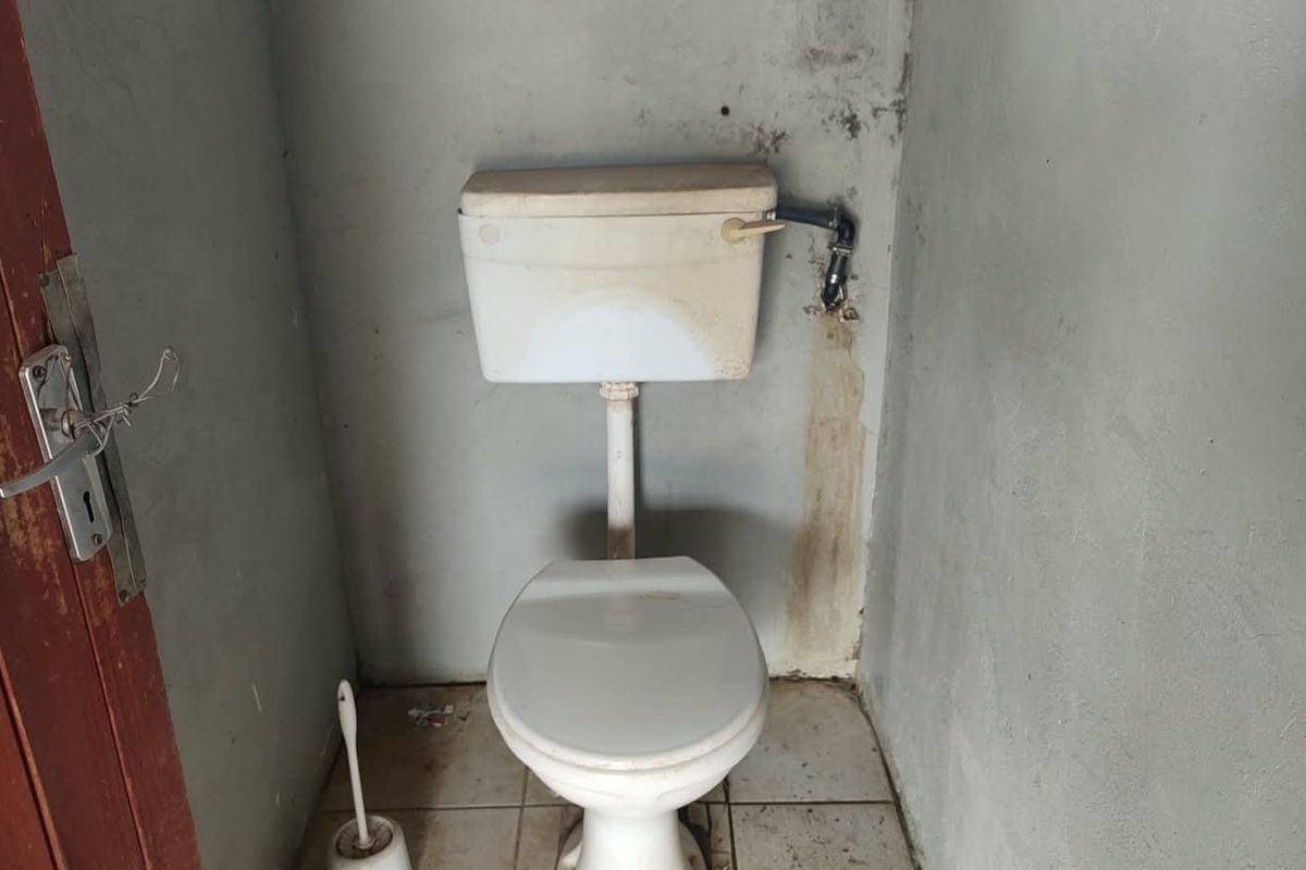 A small, basic bathroom featuring a standard toilet and cistern, requiring significant cosmetic updates and wall repairs to improve its condition.