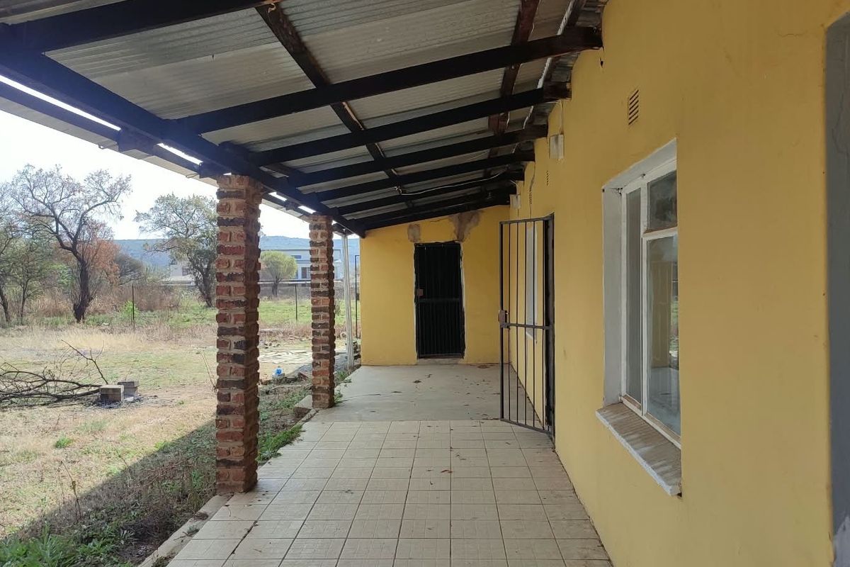 A covered outdoor patio area featuring tiled flooring, exposed brick support pillars, and a corrugated metal roof, overlooking the rear garden space.