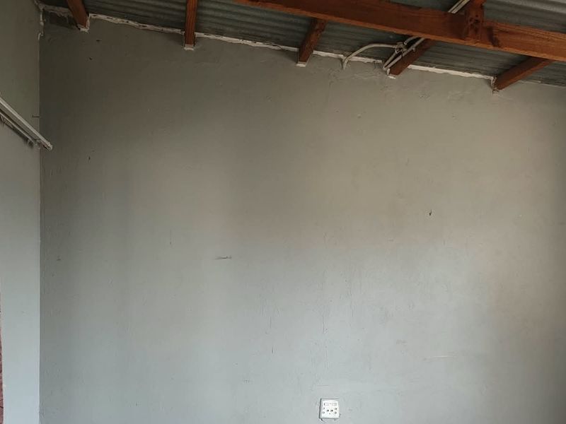 An empty bedroom featuring exposed timber rafters and corrugated metal roofing, requiring finishing touches to the ceiling and wall surfaces.