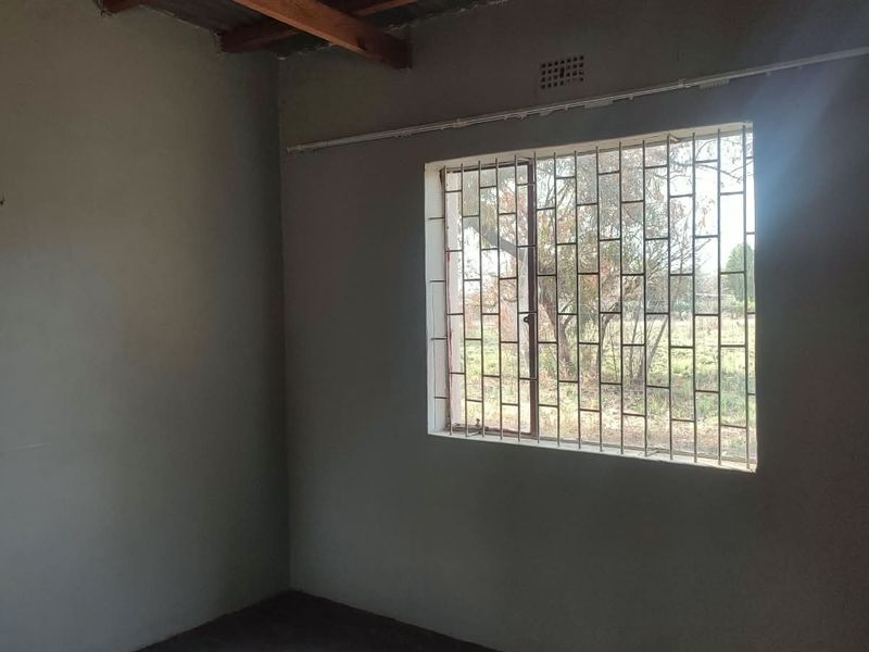 An empty bedroom featuring security bars on the window and exposed timber ceiling beams, requiring finishing touches to complete the space.