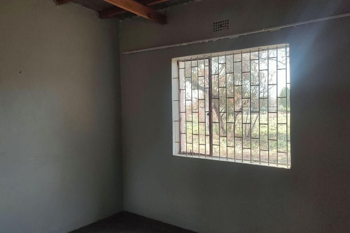 An empty bedroom featuring security bars on the window and exposed timber ceiling beams, requiring finishing touches to complete the space.