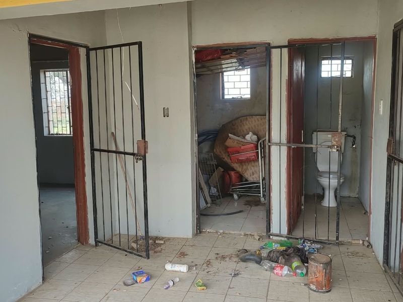 A utility area featuring tiled flooring, security gates, and a basic toilet facility, currently in need of maintenance and cleaning.