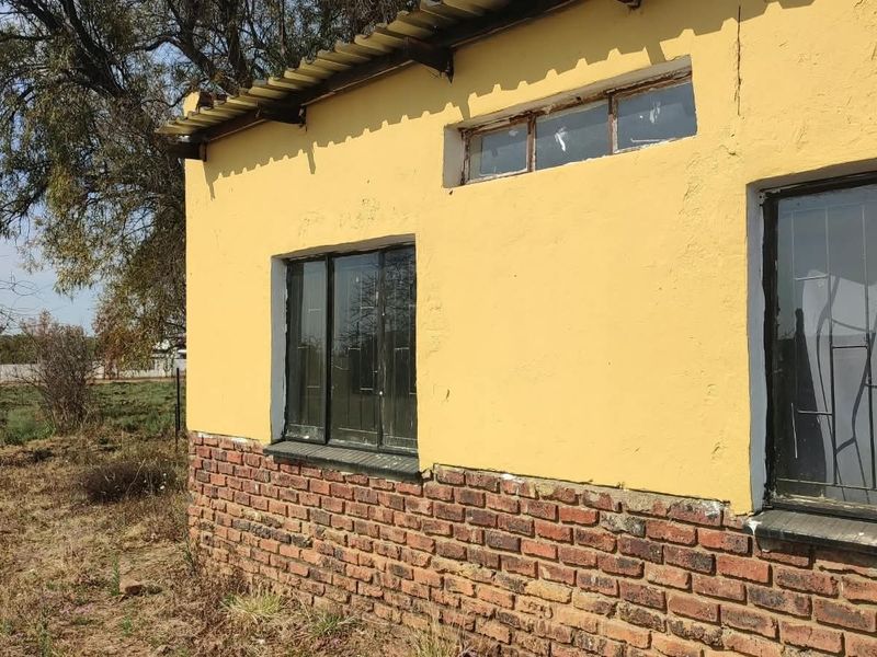 Exterior view of a building featuring a brick base, yellow plastered walls, and metal window frames, showing signs of significant wear and maintenance requirements.