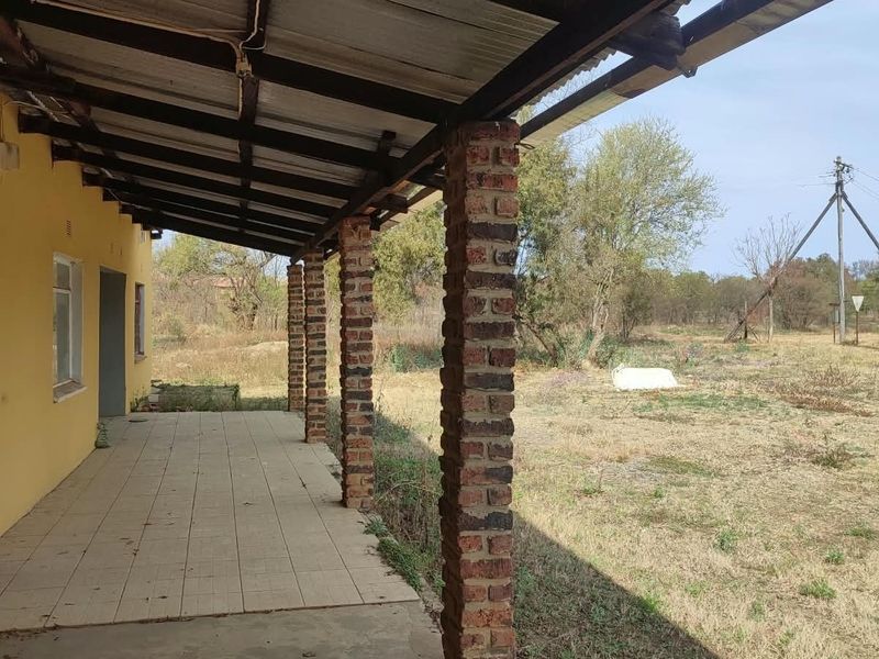 A covered outdoor patio area featuring exposed brick columns and tiled flooring, overlooking a large, open garden space.