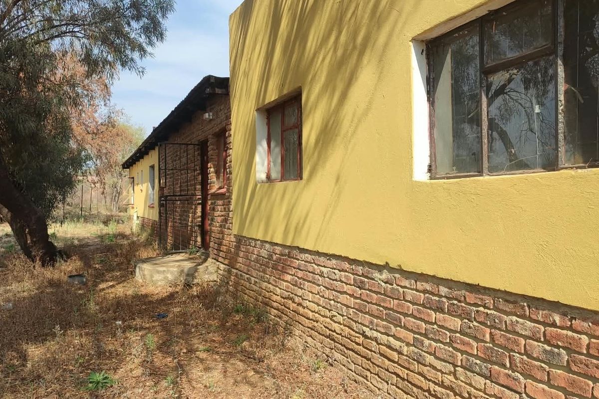 Rear exterior view of the property featuring a combination of brick and plastered walls with metal window frames and a security gate.