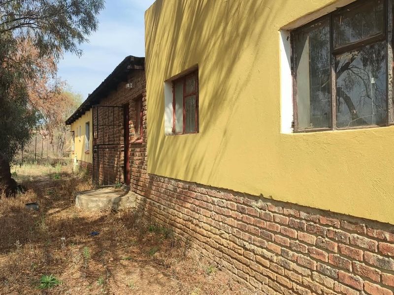 Rear exterior view of the property featuring a combination of brick and plastered walls with metal window frames and a security gate.