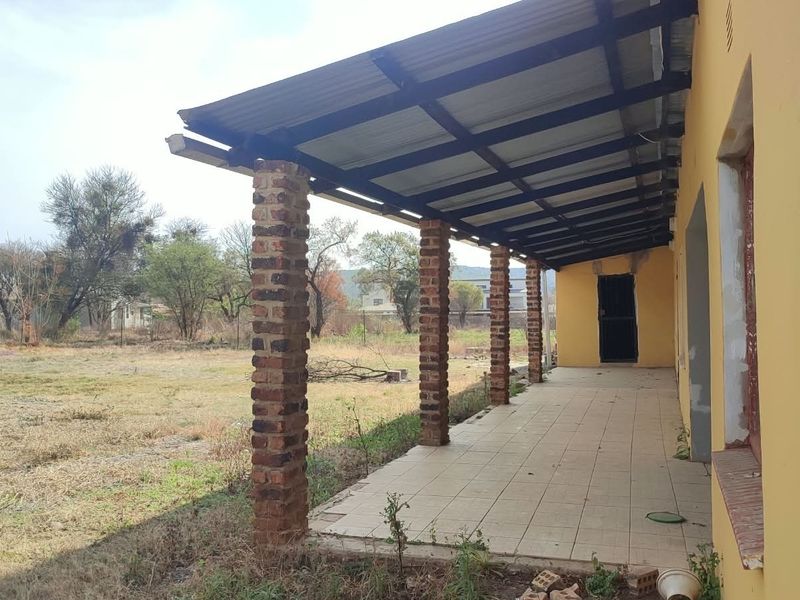 A covered outdoor patio featuring tiled flooring and exposed brick pillars, overlooking a large open garden area.