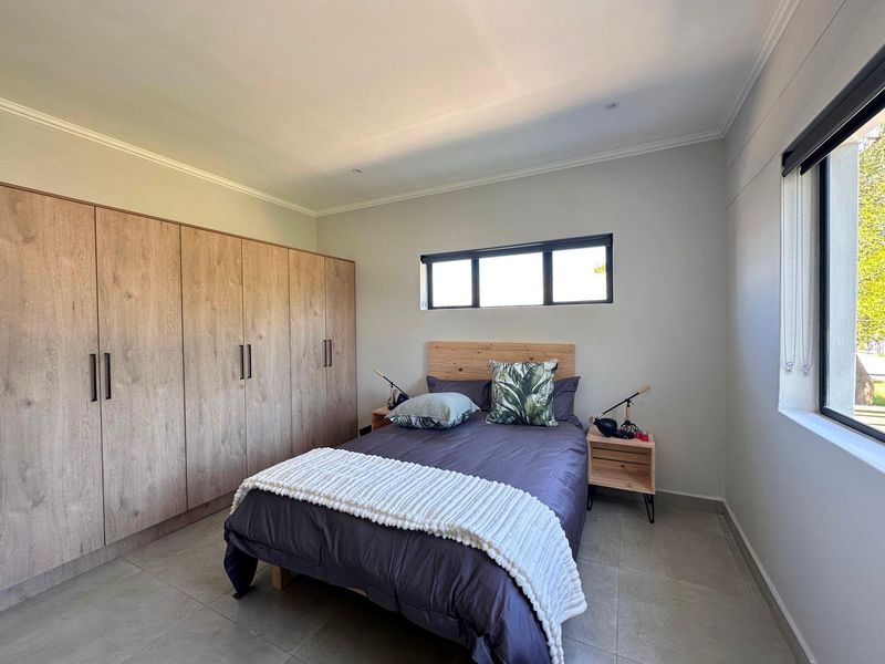 A well-maintained bedroom featuring neutral tiled flooring, built-in wooden cupboards, and a horizontal window providing natural light.