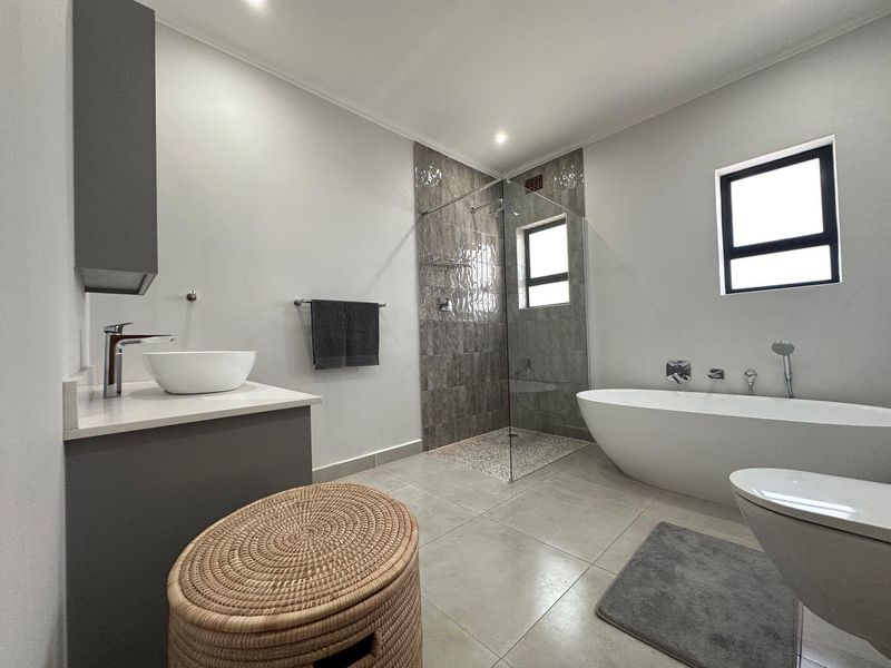 Modern bathroom featuring a sleek freestanding bathtub, a spacious walk-in shower with tiled accents, and a contemporary vanity with a vessel sink.