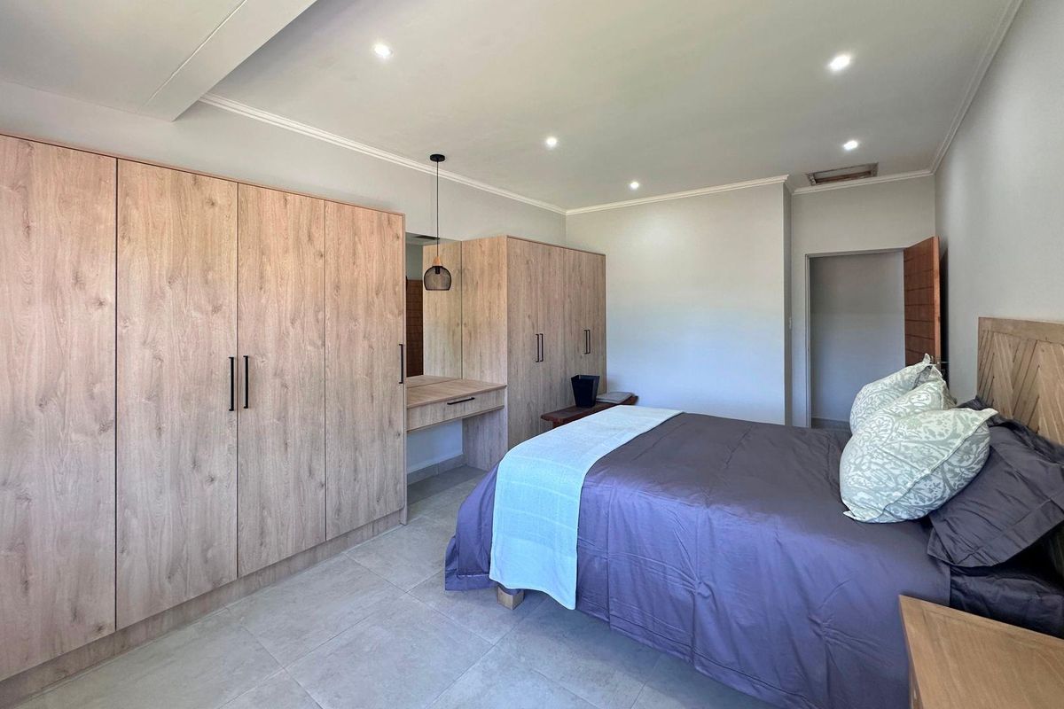 A well-maintained bedroom featuring modern light wood built-in cupboards, a matching vanity, recessed ceiling lighting, and neutral tiled flooring.