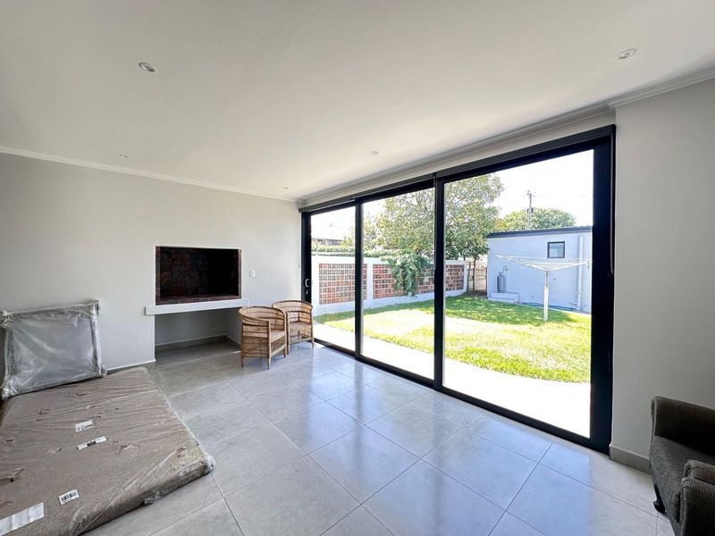 A bright, tiled indoor patio area featuring a built-in braai and large sliding glass doors that open onto the rear garden.