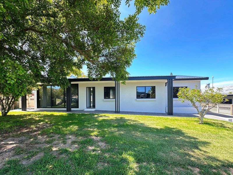 A well-maintained rear exterior view of the house featuring a paved patio, modern black-framed windows, and a spacious, manicured garden.
