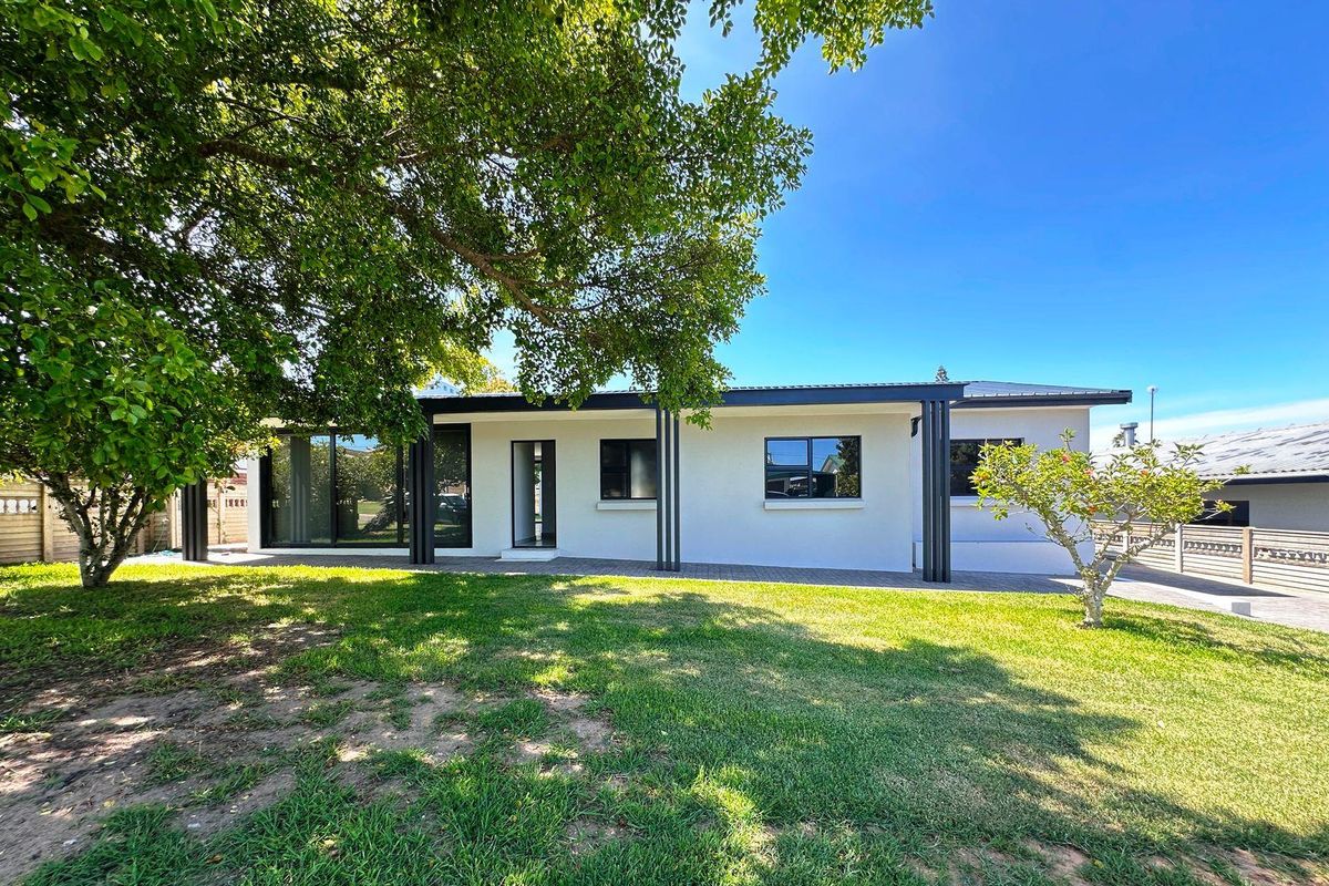 A well-maintained rear exterior view of the house featuring a paved patio, modern black-framed windows, and a spacious, manicured garden.