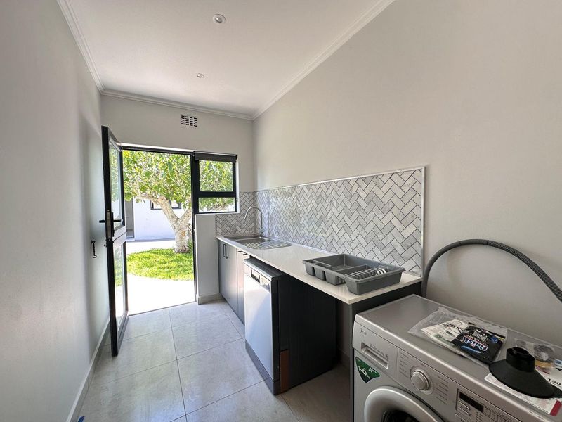 A clean, modern laundry room featuring herringbone tile backsplash, stone countertops, built-in cabinetry, and direct access to the garden.