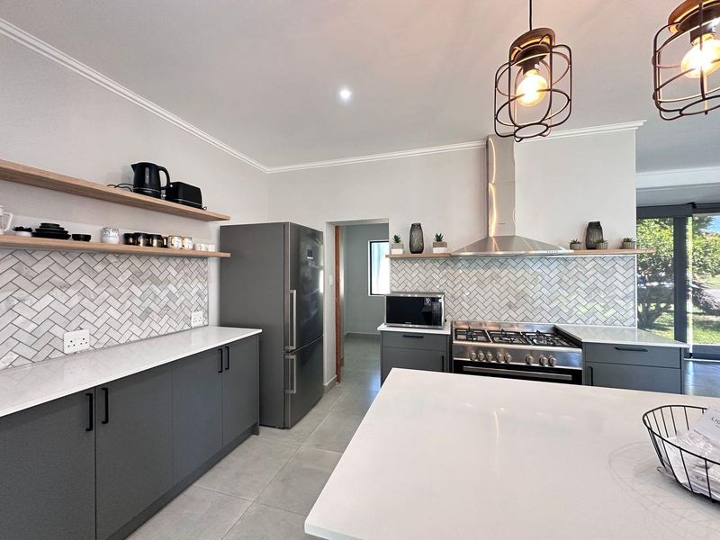 Modern kitchen featuring dark grey cabinetry, stone countertops, a herringbone tile backsplash, gas hob, and stylish pendant lighting.